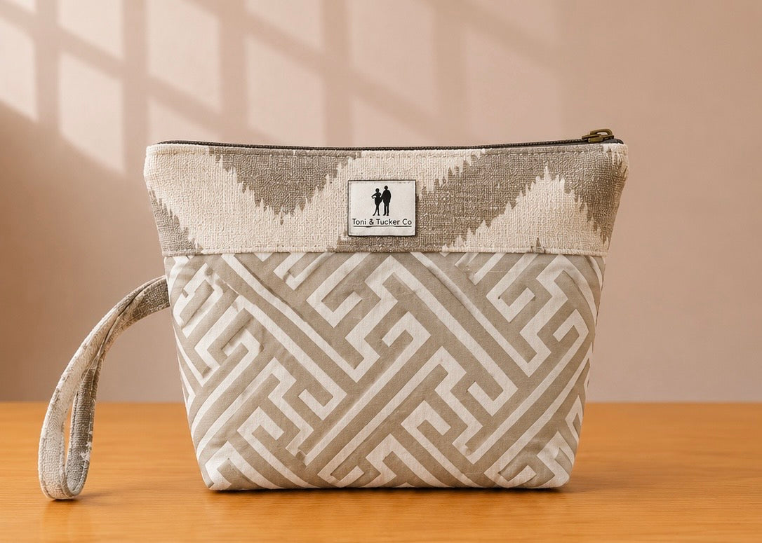 Front view of NO.011 Studio Pouch – Stone Arcade with neutral architectural patterned fabric, Toni & Tucker label, zipper closure, and wrist strap.