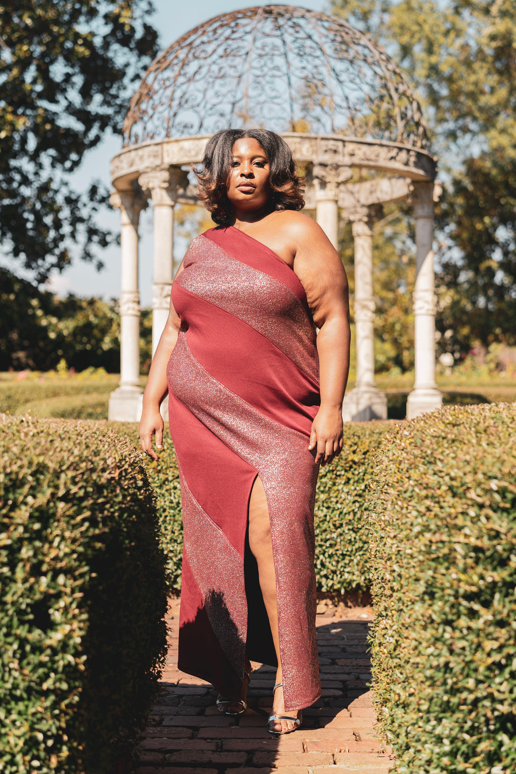 Woman in a glittery red dress standing in front of a gazebo in a garden setting