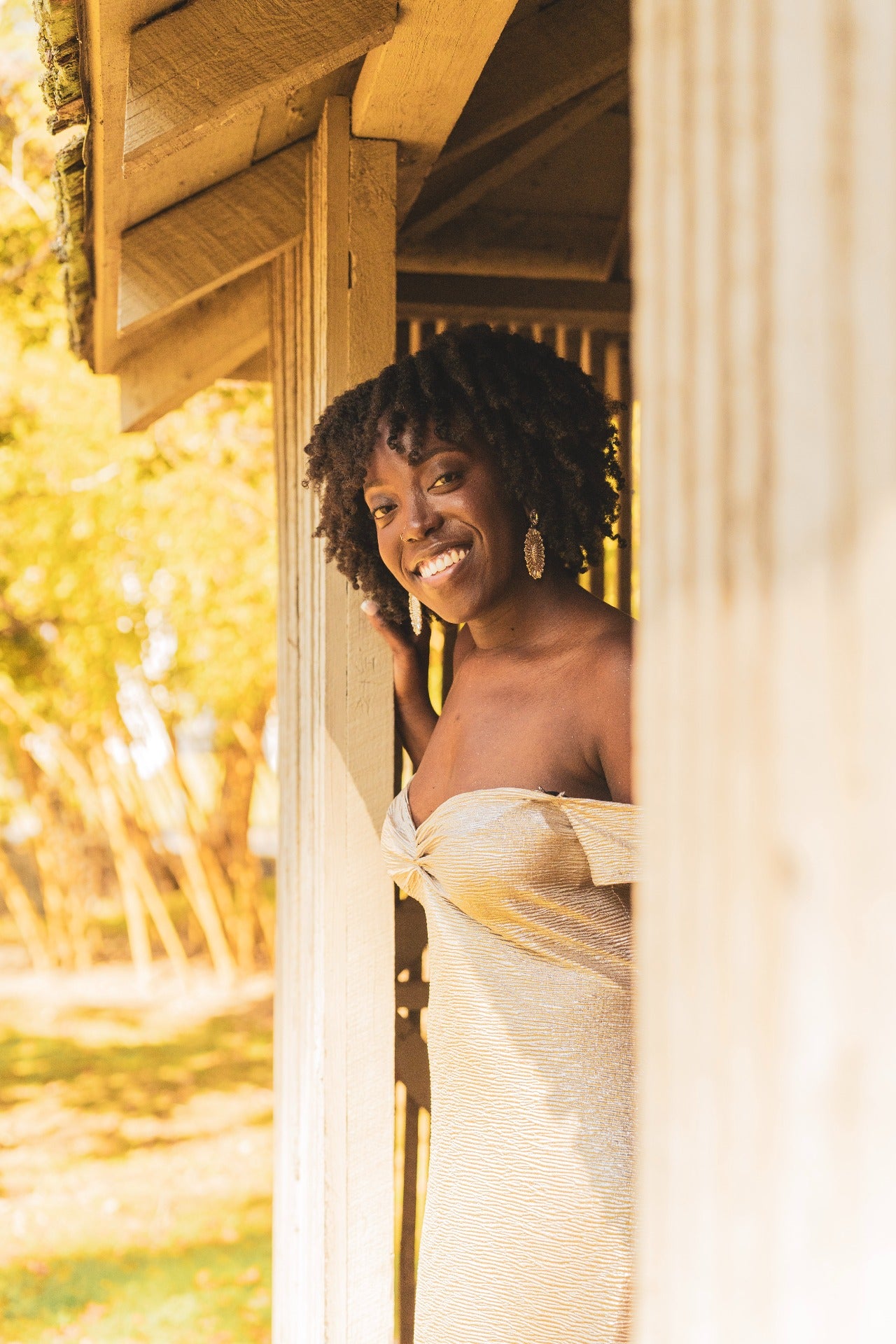 Woman standing in a metallic beige dress in a doorway with a blurred natural background