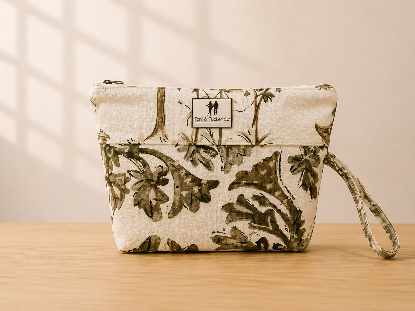 Front view of NO.002 Studio Pouch – Olive Grove with olive botanical textile, cream upper panel, exterior Toni & Tucker label, and wrist strap.