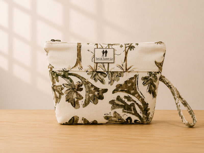 Front view of NO.002 Studio Pouch – Olive Grove with olive botanical textile, cream upper panel, exterior Toni & Tucker label, and wrist strap.