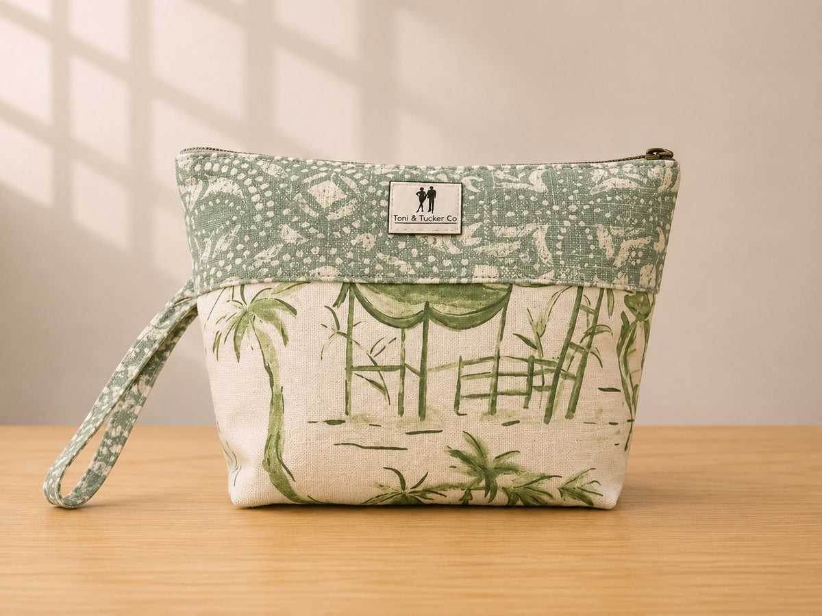 Front view of NO.004 Studio Pouch – Garden Pavilion with sage architectural textile, green garden scene panel, exterior Toni & Tucker label, and wrist strap.