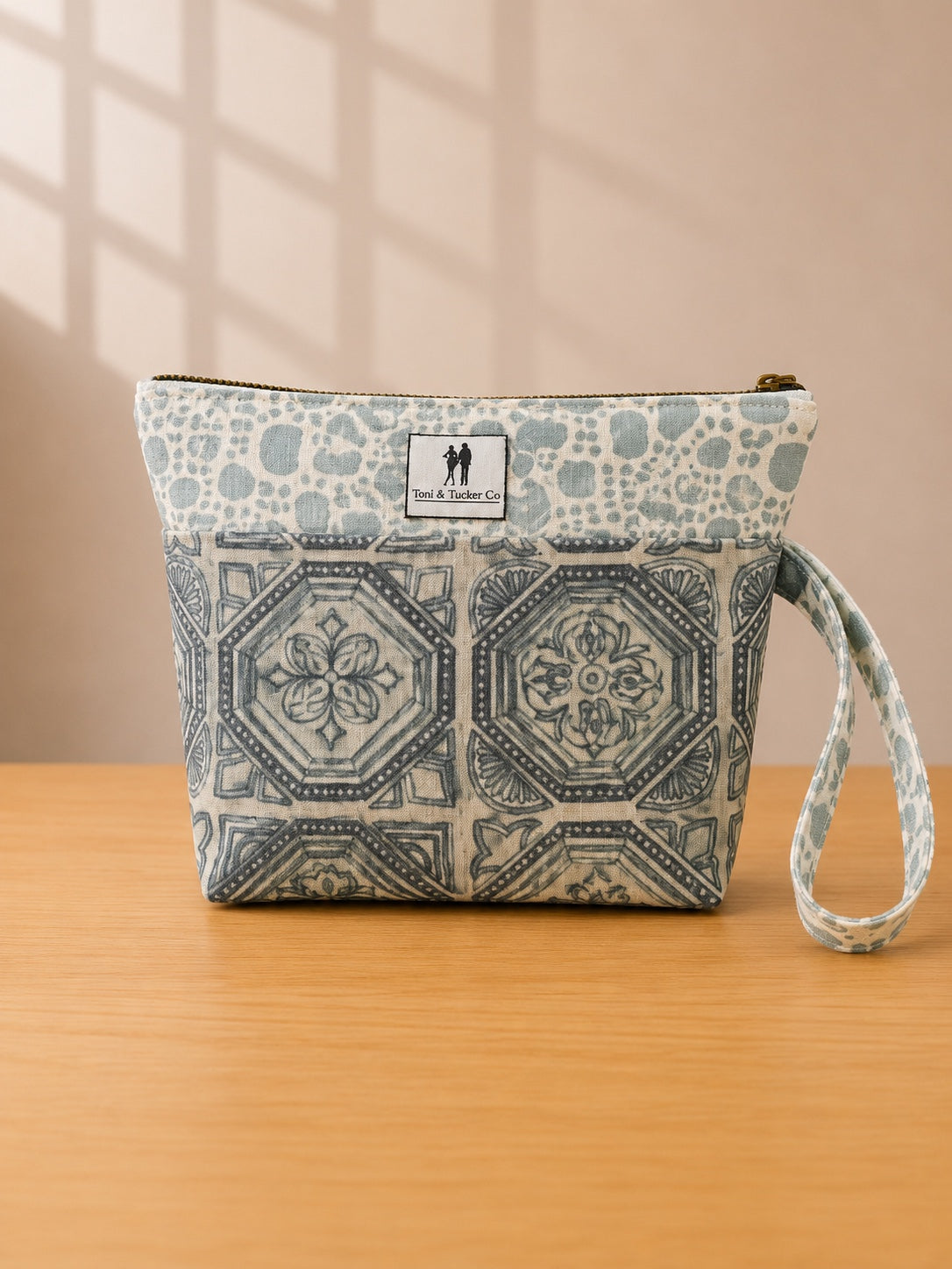 Front view of NO.007 Studio Pouch – Blue Courtyard with blue courtyard-inspired textile, exterior Toni and Tucker label, zipper closure, and wrist strap.