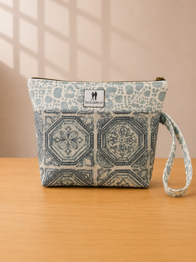 Front view of NO.007 Studio Pouch – Blue Courtyard with blue courtyard-inspired textile, exterior Toni and Tucker label, zipper closure, and wrist strap.